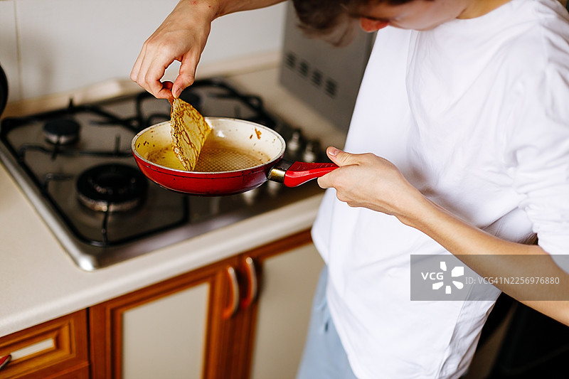 一个人在厨房里用燃气灶煎饼，手里拿着一个平底锅图片素材