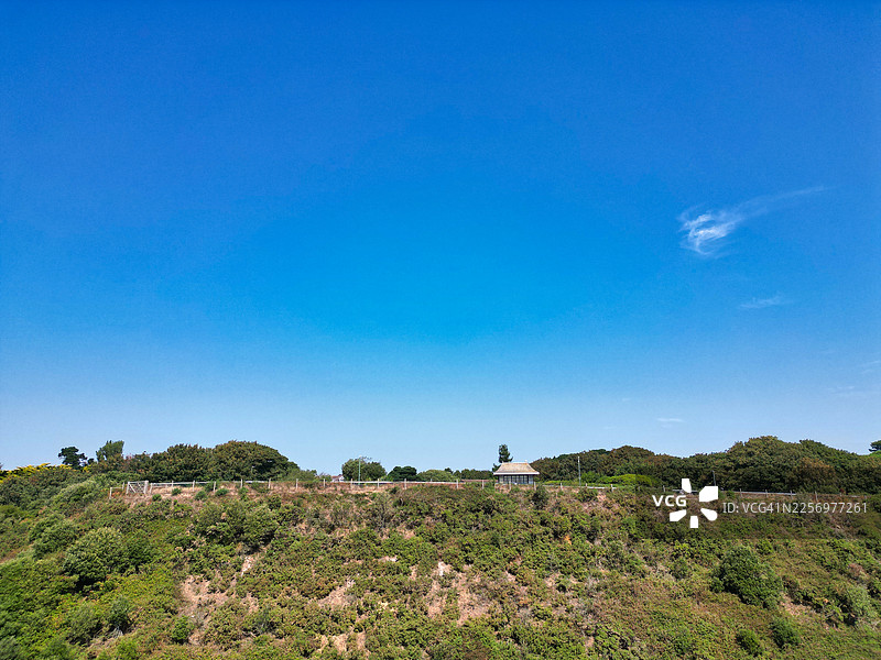 广阔的蓝天映衬着郁郁葱葱的绿色山坡，远处有一座建筑，唤起了宁静与自然之美，英国伯恩茅斯，西海岸悬崖长廊图片素材