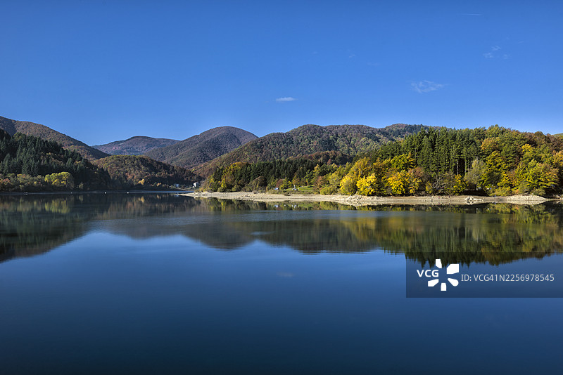 意大利卡穆尼亚诺布拉西莫内湖畔生机勃勃的秋日风光，平静湖面倒映着远山近水，天空湛蓝澄澈图片素材