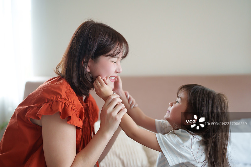 亚洲母亲在床上躺着，俏皮地捏着女儿的脸颊图片素材