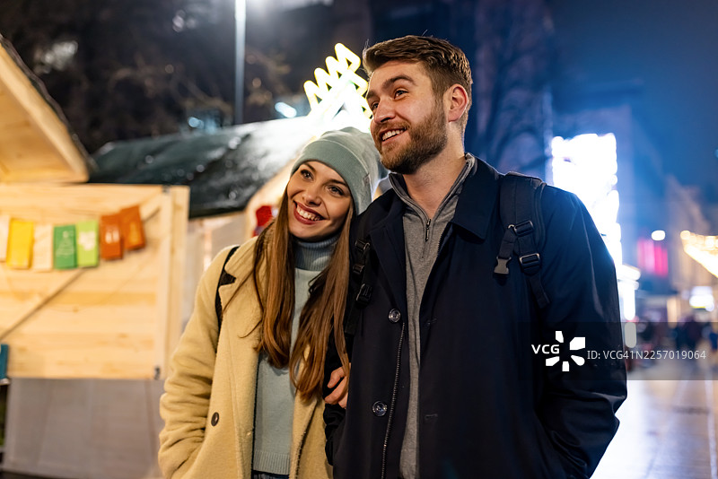 快乐情侣在夜市圣诞节，穿着暖和的外套，沐浴在节日灯光下图片素材