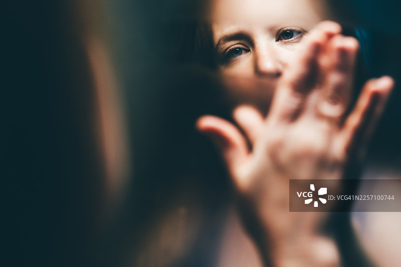 一个悲伤的女人，手放在玻璃上，看着自己的倒影。图片素材