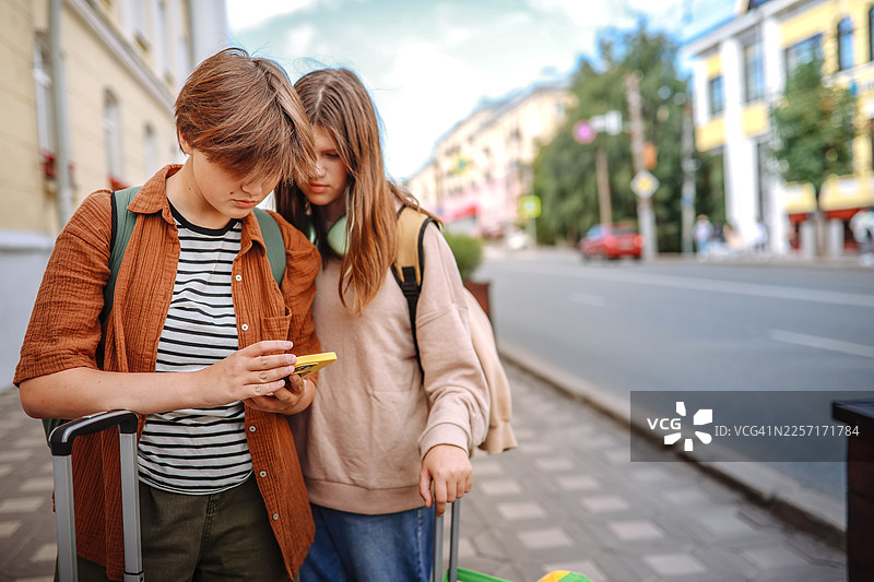 在城市街道上，几个青少年带着行李，正使用智能手机在新地方导航。图片素材