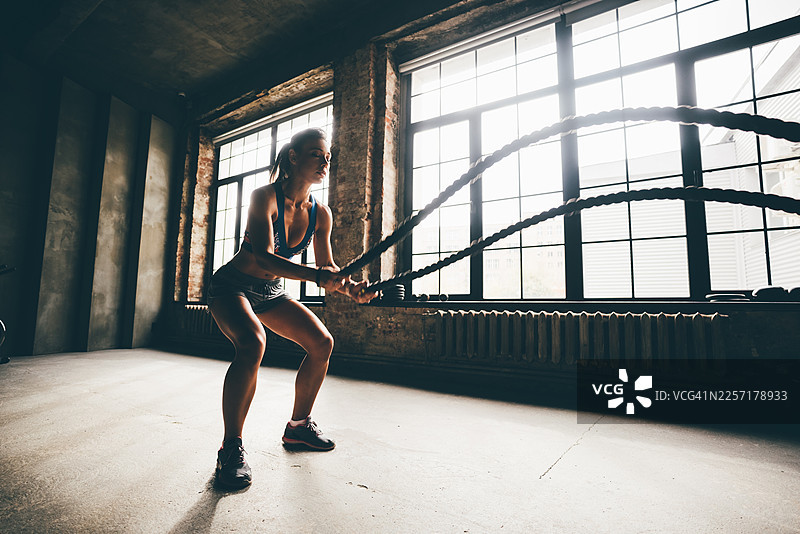 一位女性在健身房使用绳索进行训练，锻炼手臂，进行 CrossFit 有氧运动。图片素材