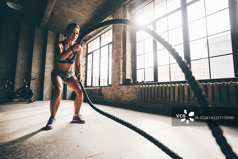 一位女性在健身房使用绳索进行训练，锻炼手臂，进行CrossFit有氧运动。图片素材