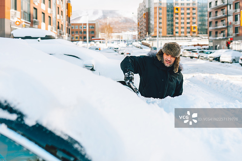 暴风雪过后，一名男子正在清理汽车挡风玻璃上的积雪图片素材