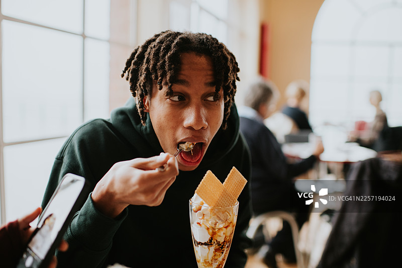 一个少年在咖啡馆里享用奢华的焦糖坚果圣代冰淇淋。图片素材