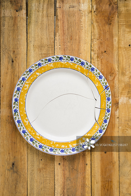 背景是木桌，上面放着一个摔碎的陶瓷盘子图片素材