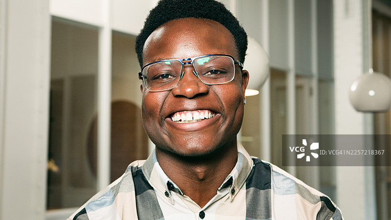 戴眼镜的微笑男士在现代室内环境中，展现自信与喜悦的肖像图片素材