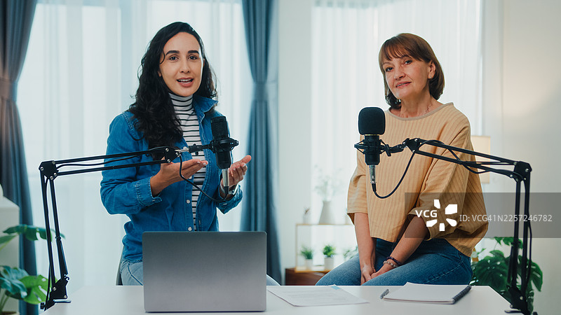 成熟的高加索女性和年轻的拉丁裔女性网红在现代家居工作室共同主持播客。直播播客节目和访谈概念。图片素材