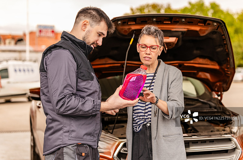下午，一对男女在加油站讨论汽车保养，并检查液体容器。图片素材