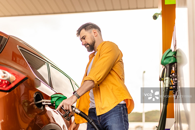 白天，一名男子在繁忙的加油站用汽油给汽车加油图片素材