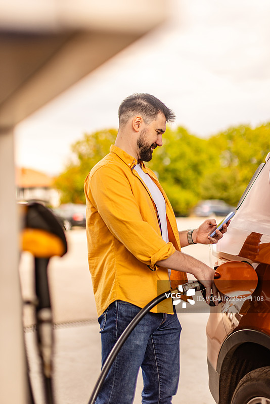 男子在下午加油站给汽车加油，同时查看手机图片素材