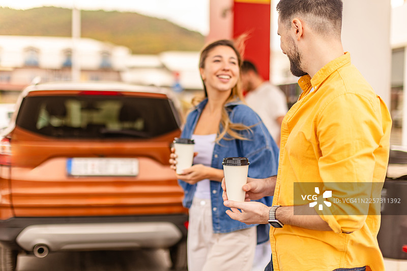 在繁忙的出行和加油日，人们在加油站为车辆加油，同时手里拿着咖啡杯。图片素材