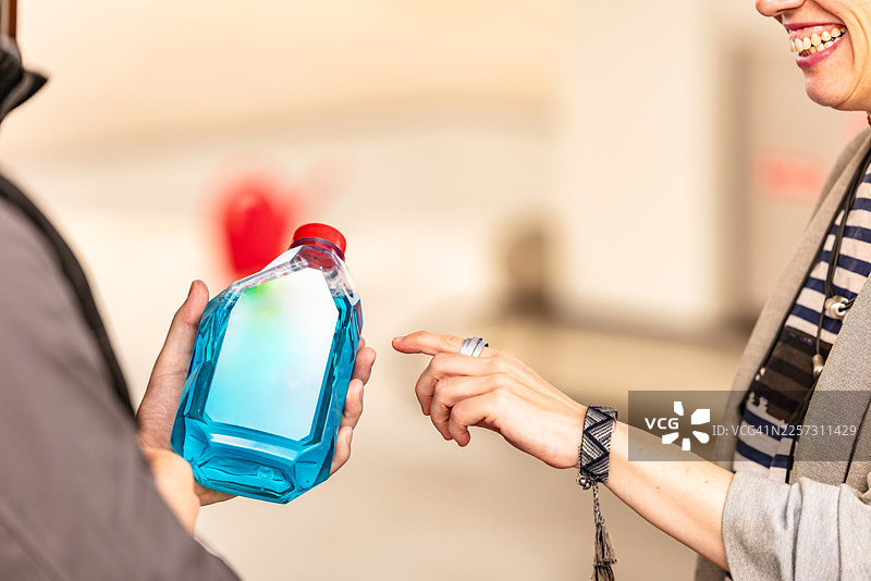 人们在加油站互动，一人拿着装有蓝色液体的瓶子，另一人指向它图片素材