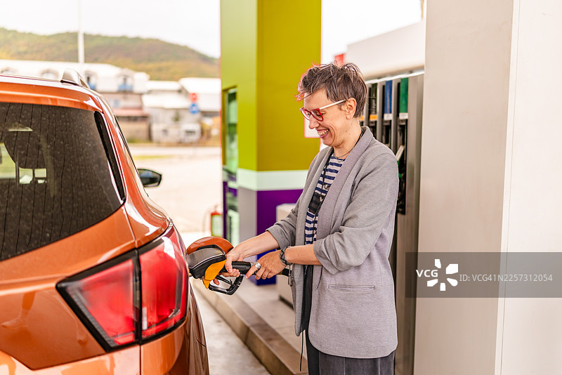 白天，人们在加油站给汽车加油，同时享受着周围繁忙的氛围和活动图片素材