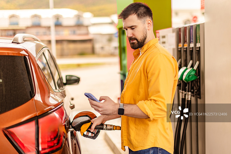在繁忙的户外场景中，边给汽车加油边查看手机图片素材