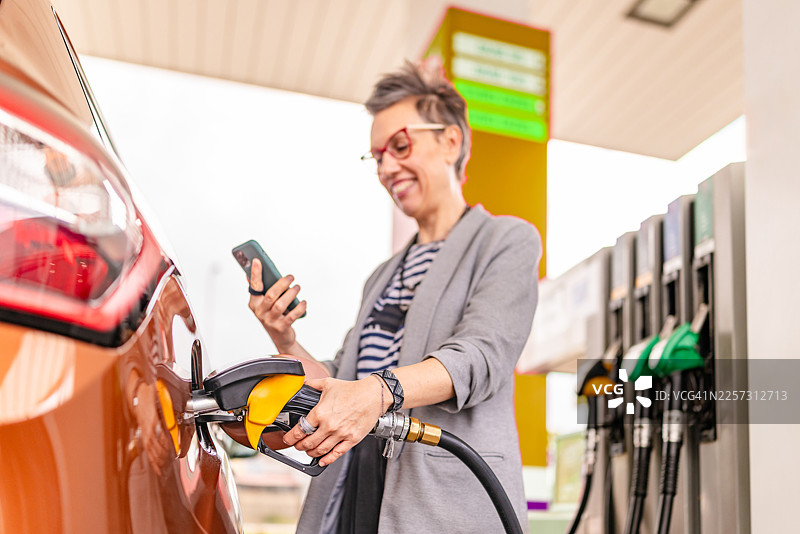 白天在户外加油站为车辆加油，同时查看手机图片素材