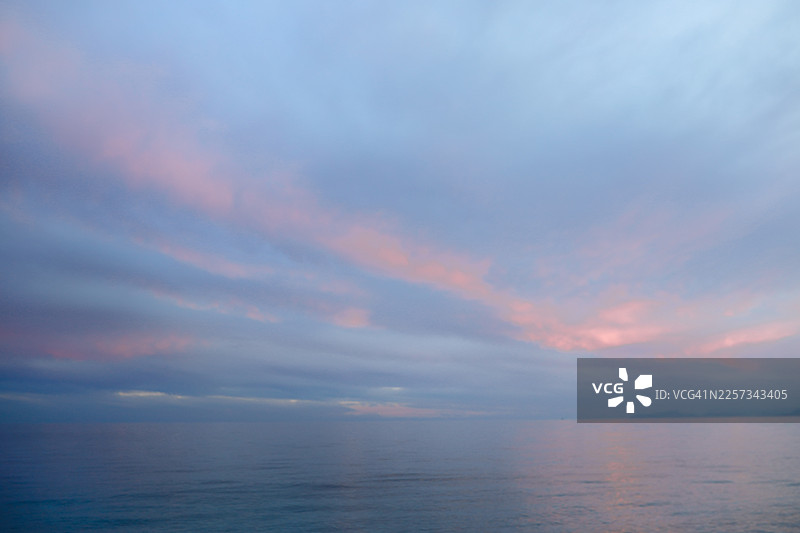 宁静与祥和：日落时分，大海与天空在柔和的蓝粉色调中融为一体。图片素材