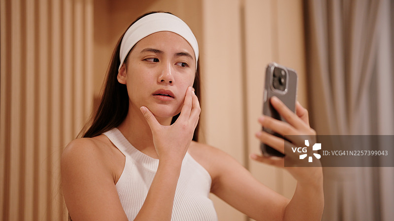 亚洲女性通过手机前置摄像头检查自己的皮肤，感到不满图片素材