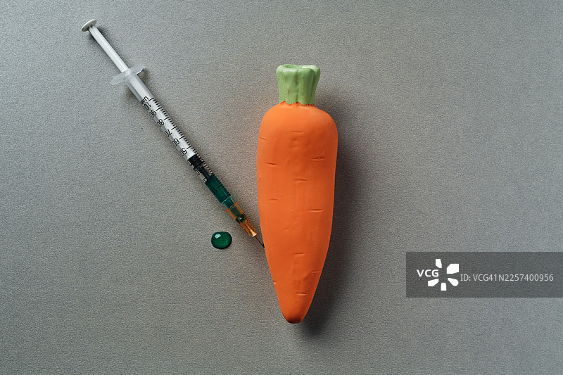 特写镜头：表面上的一根胡萝卜和一个注射器图片素材