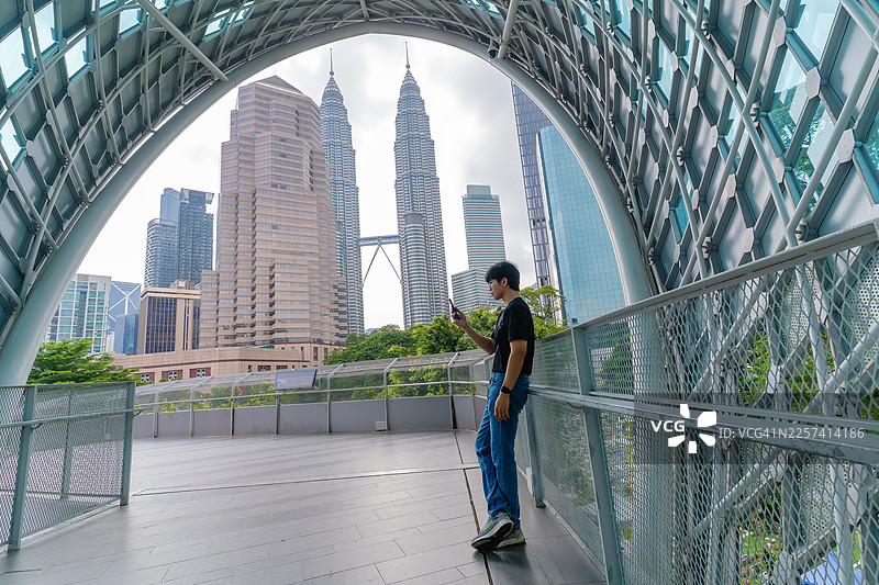 男子在沙罗玛大桥上使用手机，远眺双峰塔图片素材