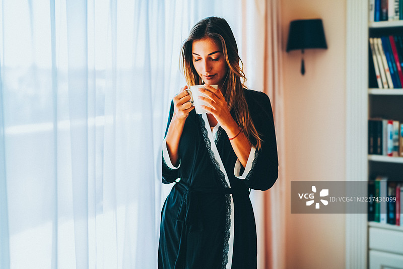 年轻女子在舒适的公寓窗边享用晨间咖啡图片素材