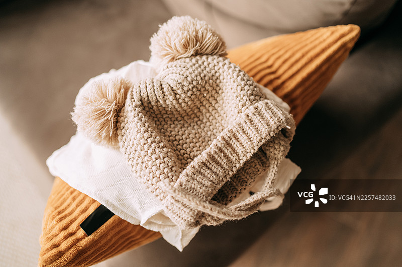 芥末色枕头上的带绒球的针织婴儿帽图片素材