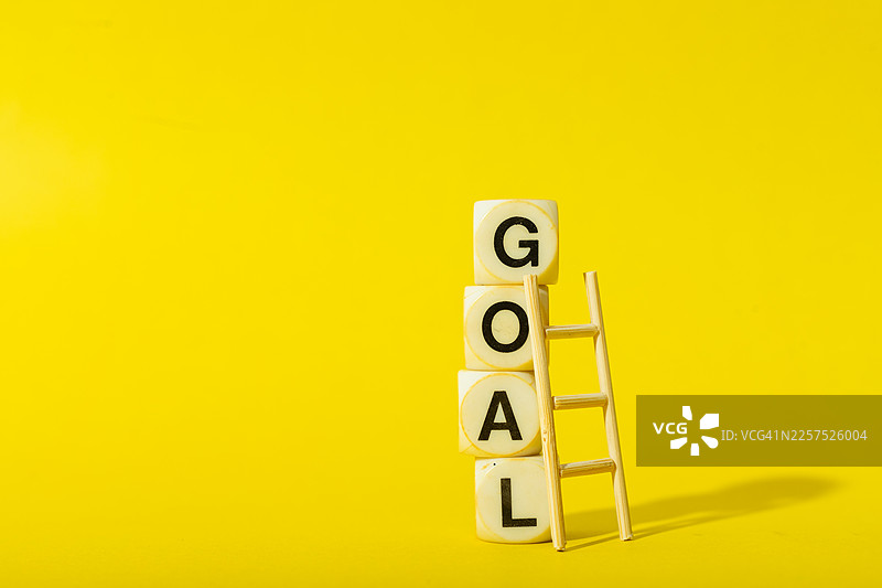 堆叠的积木，上面写着“目标”一词，旁边有一架梯子，背景为纯黄色图片素材