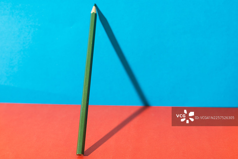 白天，一支绿色的铅笔直立在平面上，背景色彩斑斓。图片素材