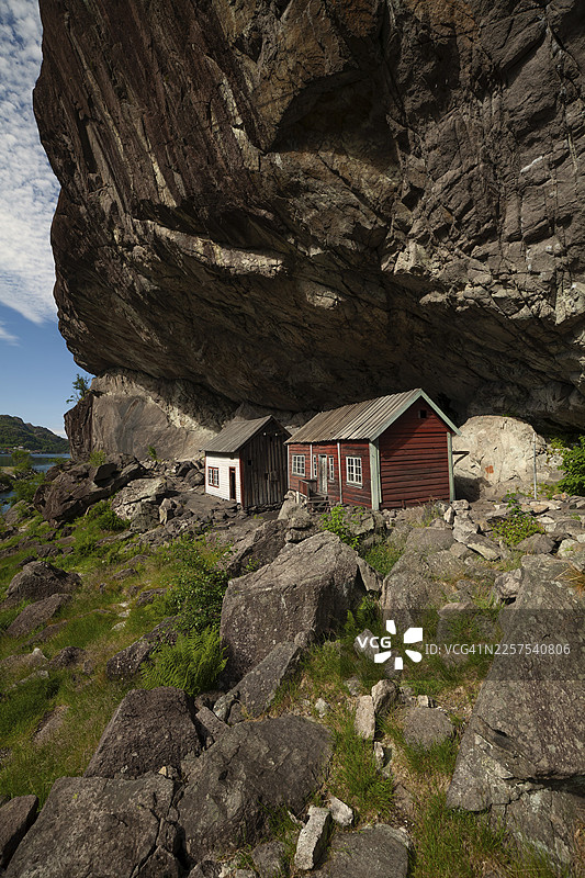 巨大的岩石悬垂下庇护着历史悠久的木屋。夏季，黑勒伦（Helleren），罗加兰，挪威图片素材