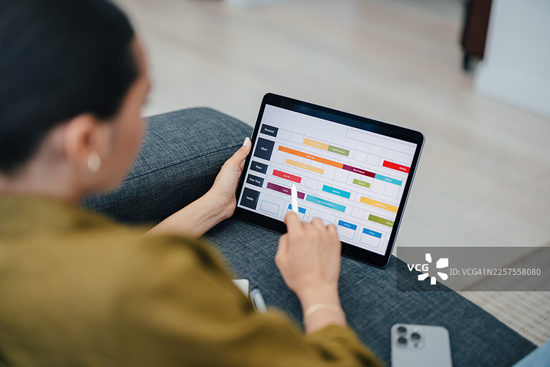 女士在家中的沙发上使用平板电脑查看多彩的日程日历图片素材