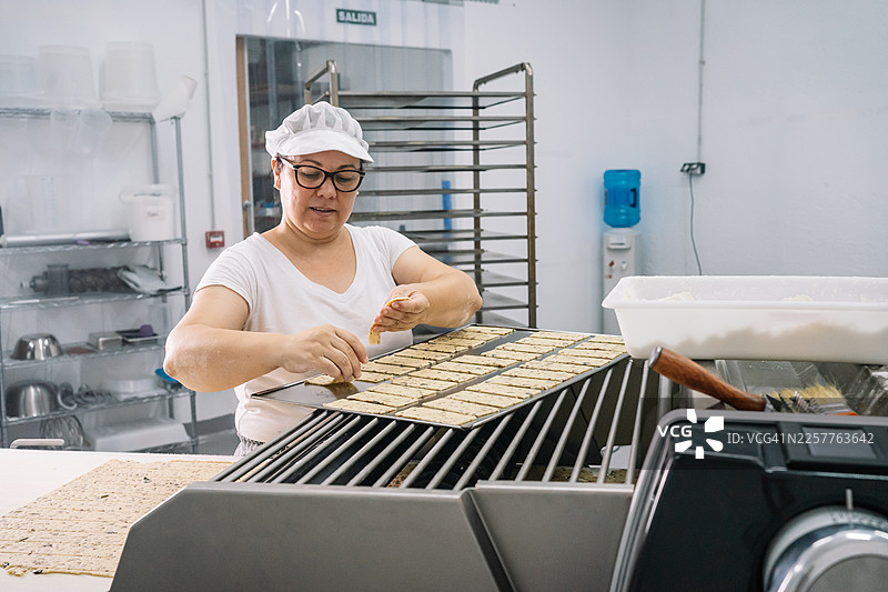 一位中年面包师将饼干放在烤盘上的广角镜头图片素材