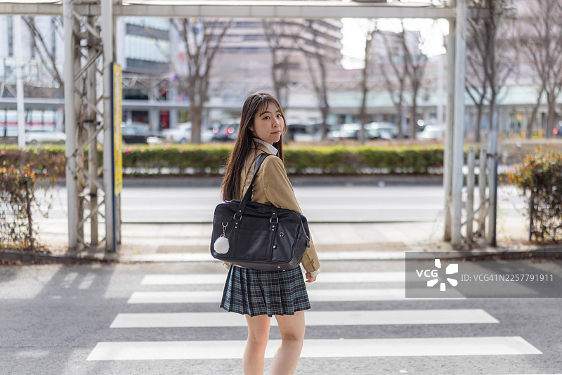 一名女高中生在去学校的路上，在公交车站回头看图片素材