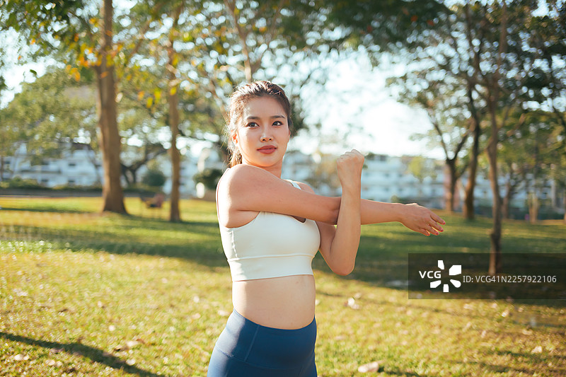 年轻女子在公园伸展手臂，为积极锻炼和健康生活方式做热身运动图片素材