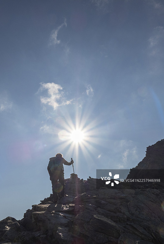 徒步者背着背包，拄着登山杖，在夕阳下攀登岩石山峰的剪影。图片素材