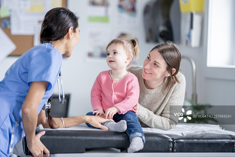 诊所里，亚裔护士与高加索母亲及孩子正在进行关怀的儿科检查图片素材