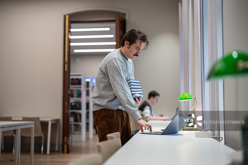 坚定的男大学生在图书馆学习，准备课程或做作业。图片素材