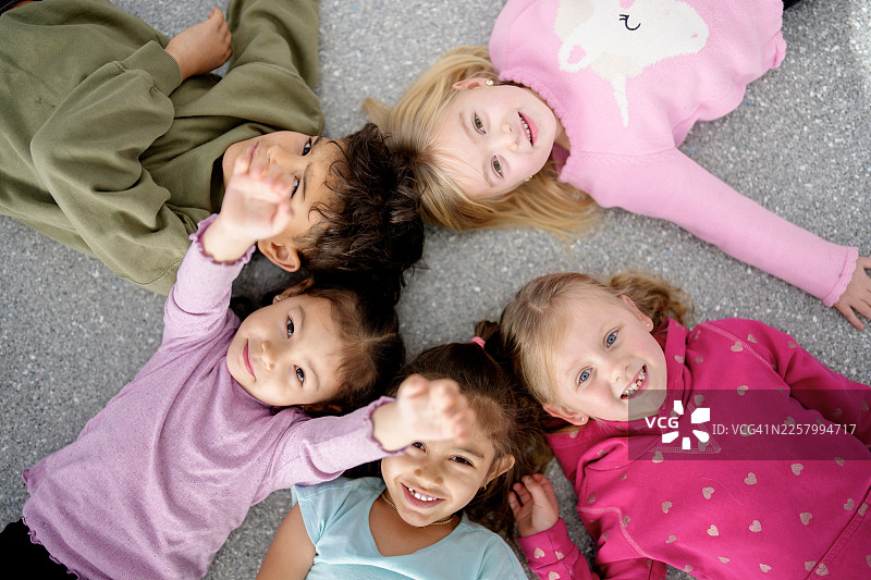 一群快乐、多元化的孩子们围成一圈躺在地上，一起微笑玩耍图片素材