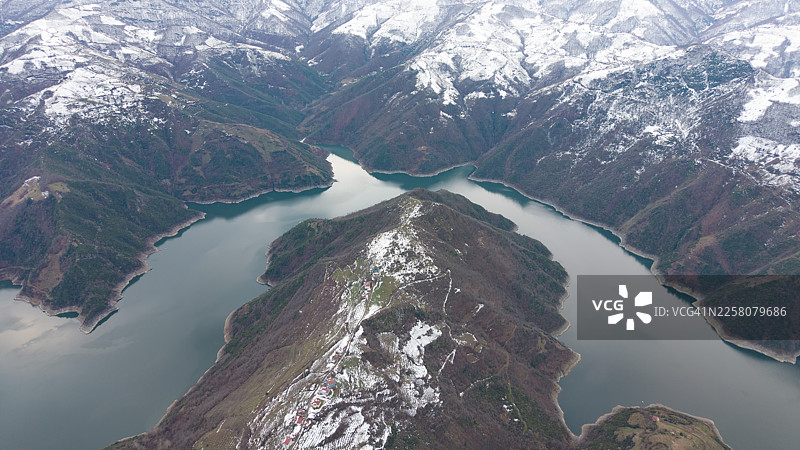 一条蜿蜒的河流穿过被白雪覆盖的山脉，天空多云图片素材