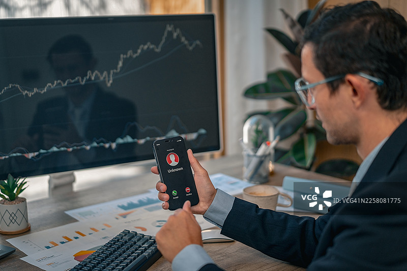 一名商人拿着一部智能手机，手机屏幕上显示着一个来自未知号码的来电。图片素材