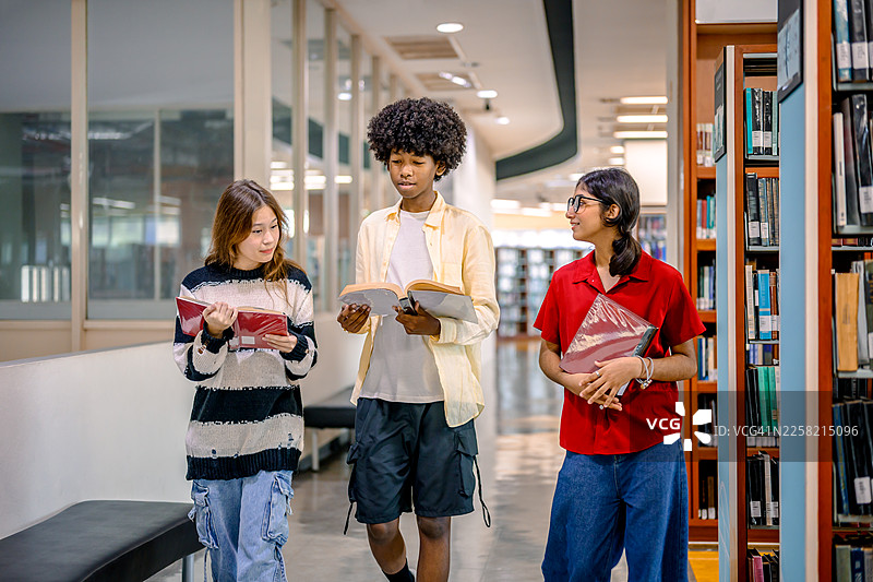 一群来自不同背景的中学生在公共图书馆里一起站着阅读课本。图片素材