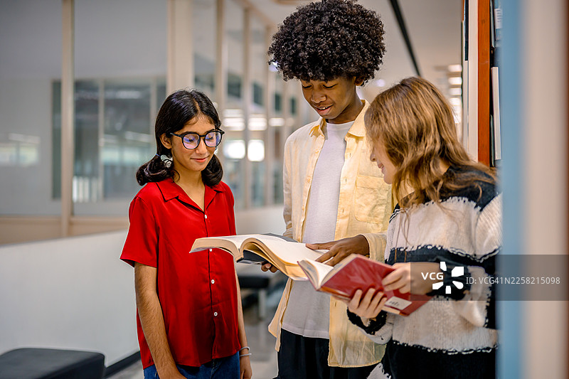 一群来自不同族裔的学生在学校图书馆的木制书架旁，一起研究和协作。图片素材