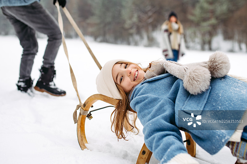 父母在冬季的自然环境中拉着女儿坐雪橇。图片素材