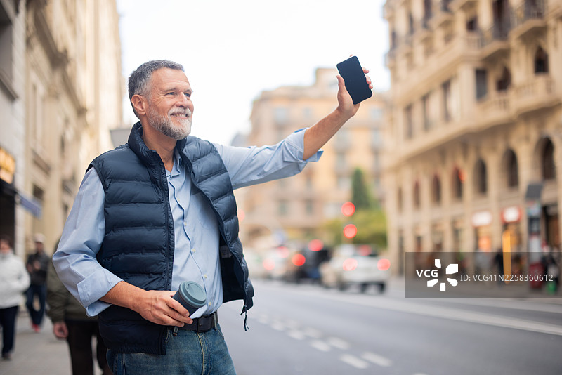 一位成熟的成年男子在城市街道上用智能手机叫车图片素材
