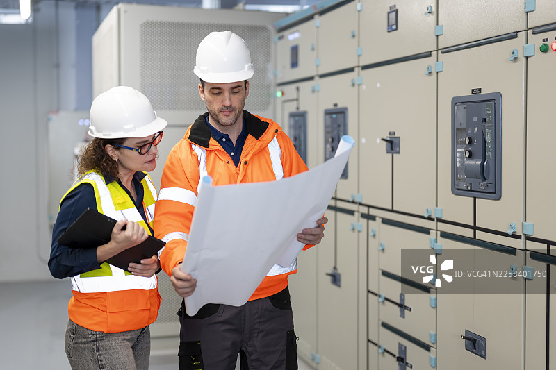 电气工程师在电气控制室现场审阅设计图纸，仔细核查承包商制作的图纸是否符合现场实际情况和技术要求。图片素材