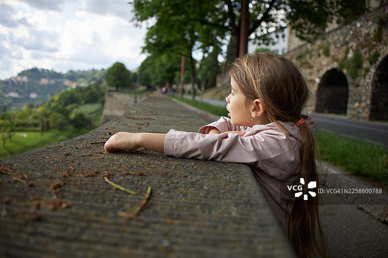 小女孩站在古老的石墙上眺望城市景观图片素材