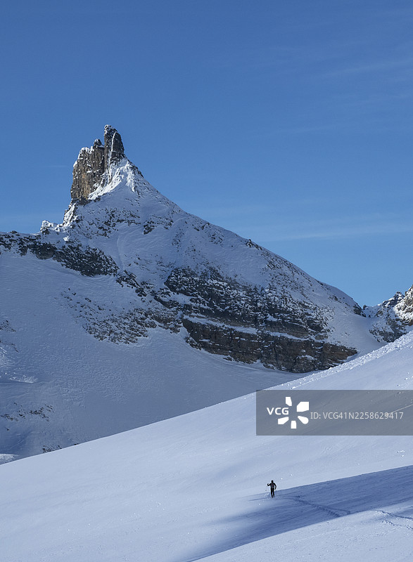 晴朗的蓝天下，滑雪者正沿着被雪覆盖的宽阔斜坡向上攀登图片素材