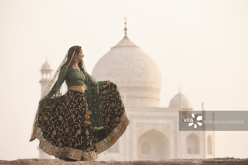 日落时分，在泰姬陵前，一位年轻女子身着纱丽，手持裙摆的侧面视角，印度北方邦阿格拉图片素材