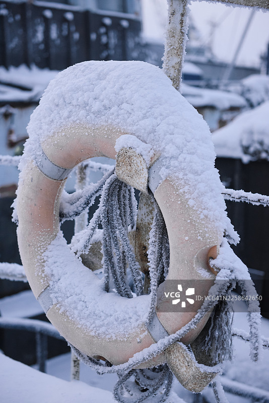 近景：一个覆盖着雪的救生圈挂在金属栏杆上，位于俄罗斯摩尔曼斯克州摩尔曼斯克图片素材